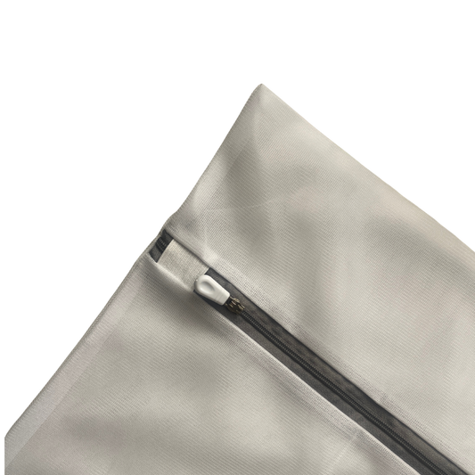 Funda de almohada de seda gris dentro de bolsa de lavado junto a detergente suave.